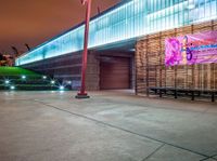 a bench and sign at the outside of a building at night with street lights all around