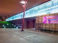 a bench and sign at the outside of a building at night with street lights all around