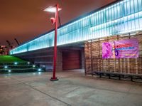 a bench and sign at the outside of a building at night with street lights all around