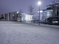 people are walking in the snow on a snowy road at night and an old building with lights