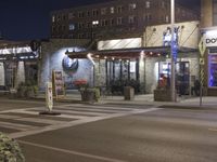 a street corner at night with an advertisement for a bar and cafe on it's sidewalk