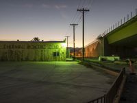 an empty parking lot at night with the sun setting behind it and an illuminated building