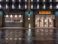 a large brick sidewalk with a store front at night time and a sign that says