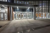 a photo of an empty building with large entrance at night with people walking by it