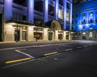 a street lit up in blue lighting and some buildings at night time and a road with parking meters between it