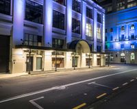 a street lit up in blue lighting and some buildings at night time and a road with parking meters between it