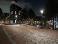 a brick path with many bikes next to a building and street light at night outside