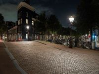 a brick path with many bikes next to a building and street light at night outside