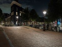 a brick path with many bikes next to a building and street light at night outside