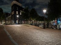 a brick path with many bikes next to a building and street light at night outside