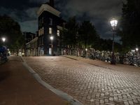 a brick path with many bikes next to a building and street light at night outside