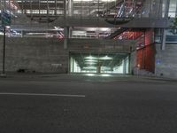 a empty parking garage under an indoor bridge on a city street at night time, in the middle of a wide street