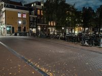 bicycles are parked along the edge of a walkway on a night time sidewalk near a building