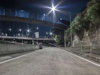 an empty road is pictured with bright lights in the distance at night near a hill