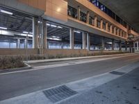 an empty road by a large building at night near a sidewalk with a paved roadway