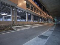 an empty road by a large building at night near a sidewalk with a paved roadway