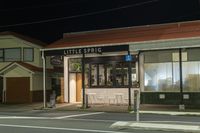 a street at night with a cafe in the corner and a bus coming out of it