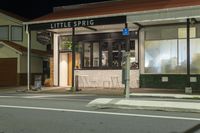 a street at night with a cafe in the corner and a bus coming out of it