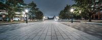 an empty sidewalk is in a city at night with many lights on them and trees