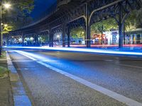 cars driving down a city street next to tall buildings at night, and a bridge