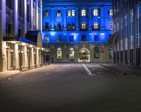 a blue building is seen from a dark street at nighttime with empty streets and parking spots