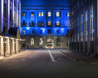 a blue building is seen from a dark street at nighttime with empty streets and parking spots