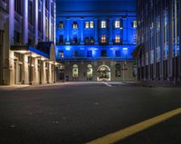 a blue building is seen from a dark street at nighttime with empty streets and parking spots