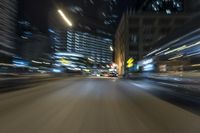 a blurry photograph shows a city street during the night with cars and street lights