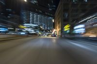 a blurry photograph shows a city street during the night with cars and street lights