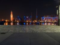 an area with buildings, lights and people walking through it near a lake at night