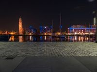 an area with buildings, lights and people walking through it near a lake at night