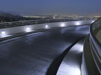 a circular walkway lit up with bright lights above a city at night time with urban buildings in the distance