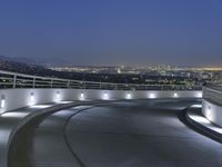 a circular walkway lit up with bright lights above a city at night time with urban buildings in the distance