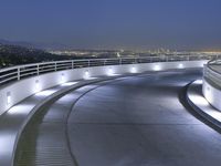 a circular walkway lit up with bright lights above a city at night time with urban buildings in the distance