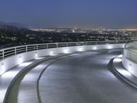 a circular walkway lit up with bright lights above a city at night time with urban buildings in the distance