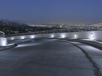 a circular walkway lit up with bright lights above a city at night time with urban buildings in the distance