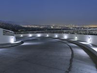 a circular walkway lit up with bright lights above a city at night time with urban buildings in the distance