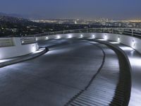 a circular walkway lit up with bright lights above a city at night time with urban buildings in the distance