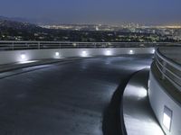 a circular walkway lit up with bright lights above a city at night time with urban buildings in the distance