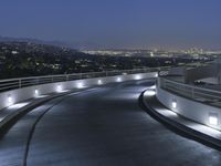 a circular walkway lit up with bright lights above a city at night time with urban buildings in the distance