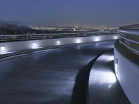 a circular walkway lit up with bright lights above a city at night time with urban buildings in the distance