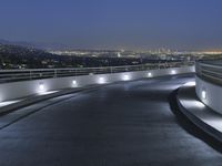 a circular walkway lit up with bright lights above a city at night time with urban buildings in the distance