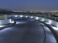 a circular walkway lit up with bright lights above a city at night time with urban buildings in the distance