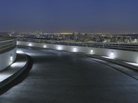 a circular walkway lit up with bright lights above a city at night time with urban buildings in the distance