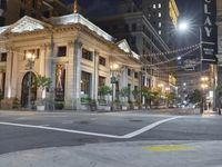 a city street corner at night with cars passing by and buildings on either side of the street