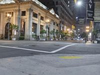 a city street corner at night with cars passing by and buildings on either side of the street