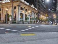 a city street corner at night with cars passing by and buildings on either side of the street