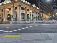 a city street corner at night with cars passing by and buildings on either side of the street