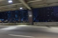 a car driving on the street at night with tall buildings in the background and two lights on and the vehicle is going through the intersection