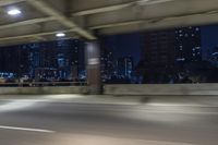 a car driving on the street at night with tall buildings in the background and two lights on and the vehicle is going through the intersection